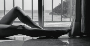 A woman's legs on a balcony with a cliffside and coastline behind her.