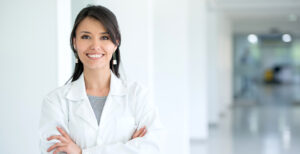 A female doctor in a white coat smiling and crossing her arms.