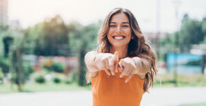 A woman smiling with her arms raised and fingers pointing forwards.
