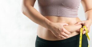 Woman grabbing the side of her stomach and grabbing skin, while holding a measuring tape