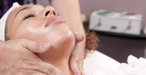woman laying down with her eyes closed while receiving a facial