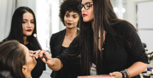 woman putting makeup on someone and students learning through a school for makeup artist