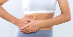 woman in a white crop top and grey pants with both of her hands on her side stomach pressing down