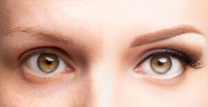 womans eyes, one side is natural while the other side has makeup and microblading done to her eyebrows