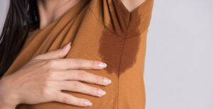 woman wearing an orange shirt with her arm up and sweating under her armpit